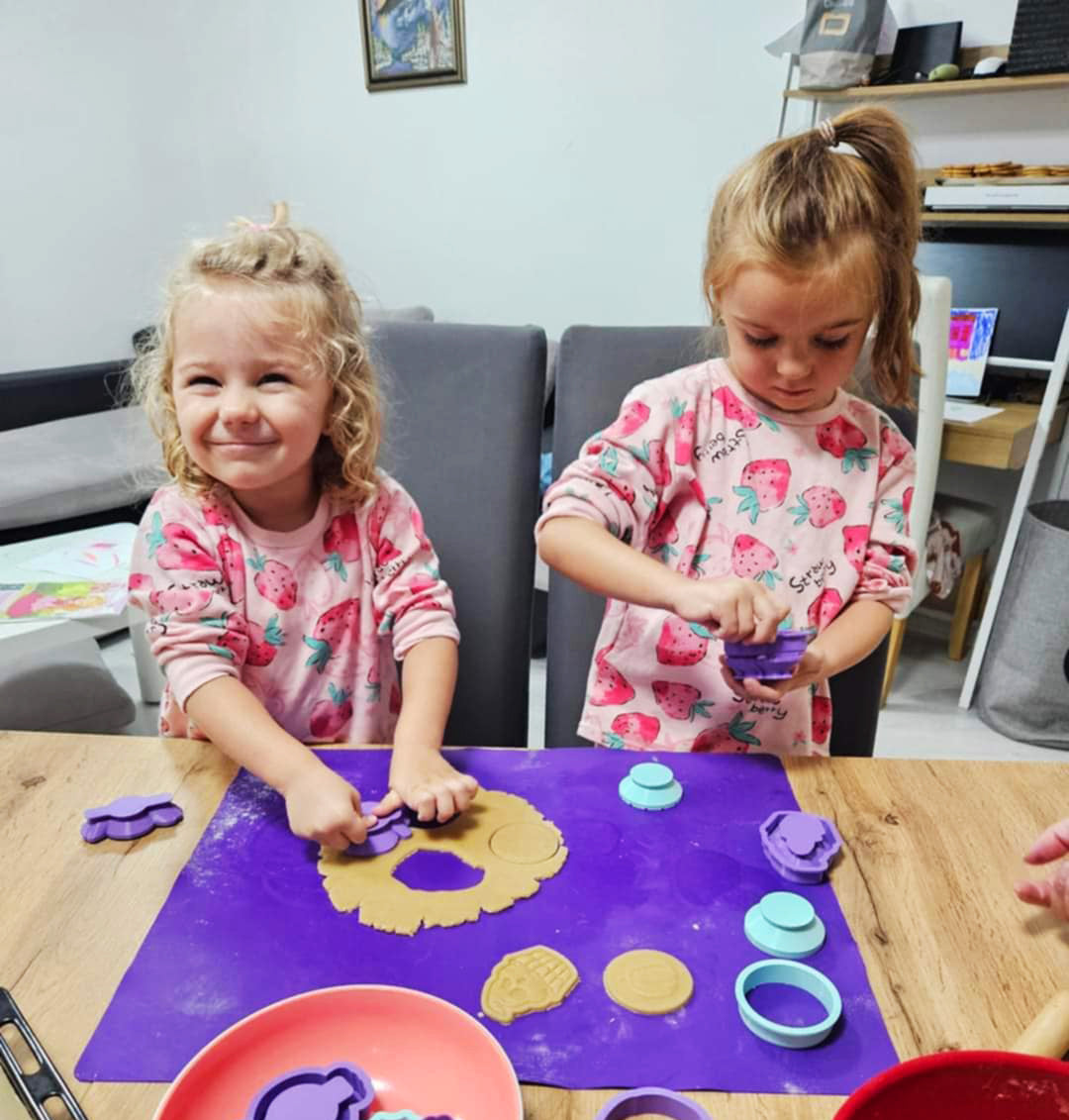 Two cute girls preparing cookies with Formini cookie cutters and stamps. One is pressing a stamp into a rolled out cookie dough.