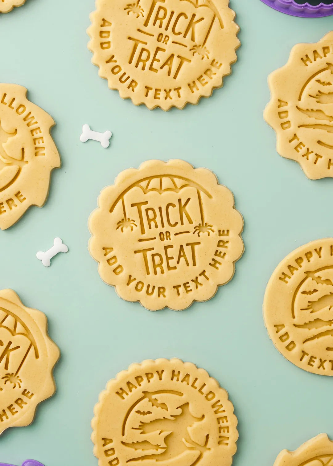 Personalizable Halloween cookies with customizable text on a light blue background. Center cookie is "trick of treat" design with custom text below it.