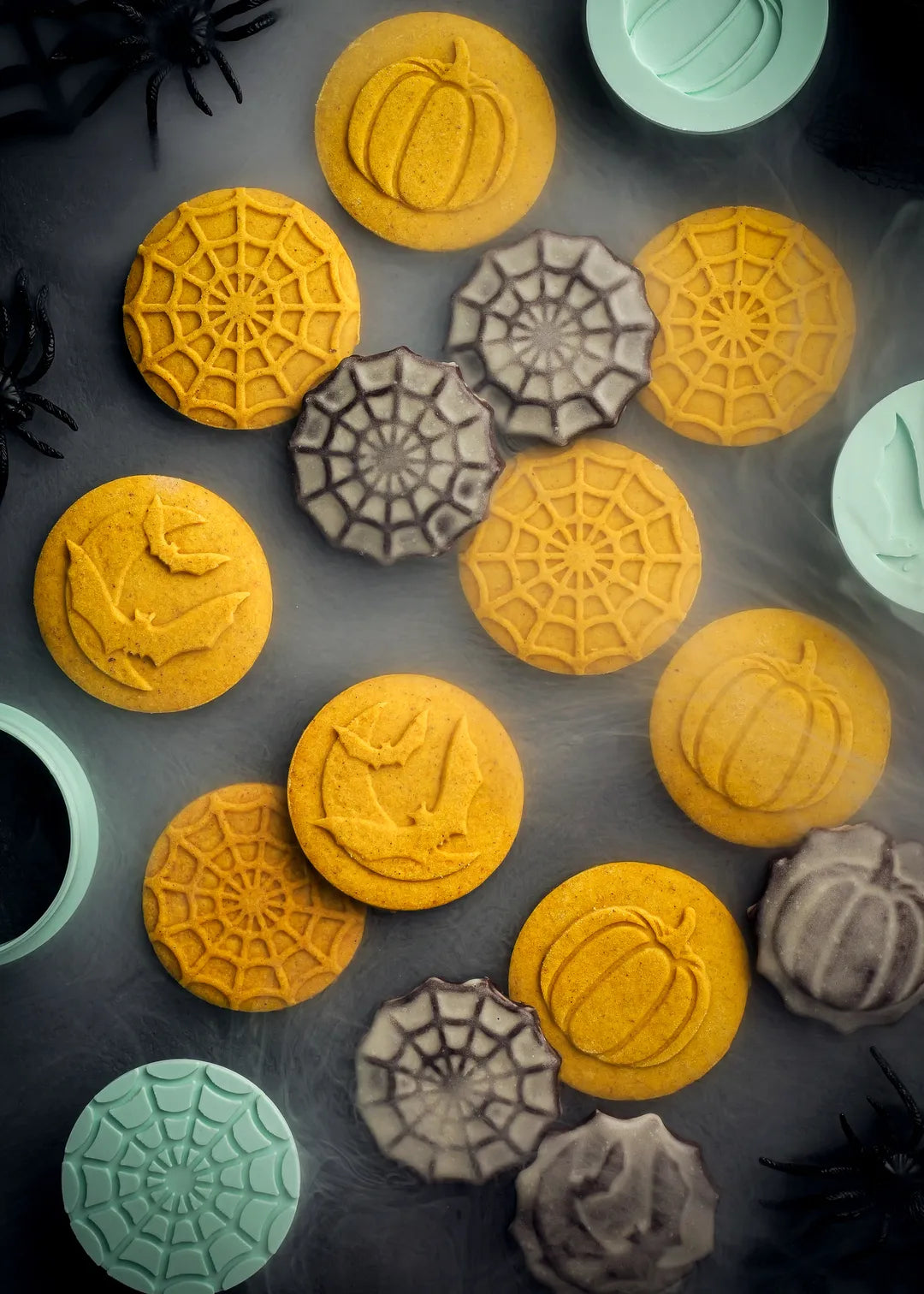 Halloween Spooky Cookie Set includes 3 cookie stamps and 2 cookie cutters. Cookie stamps feature pumpkin, spiderweb and flying bats with moon designs. The stamps create raised 3d cookie patterns. Photo of cookies made with the stamps in a creepy set