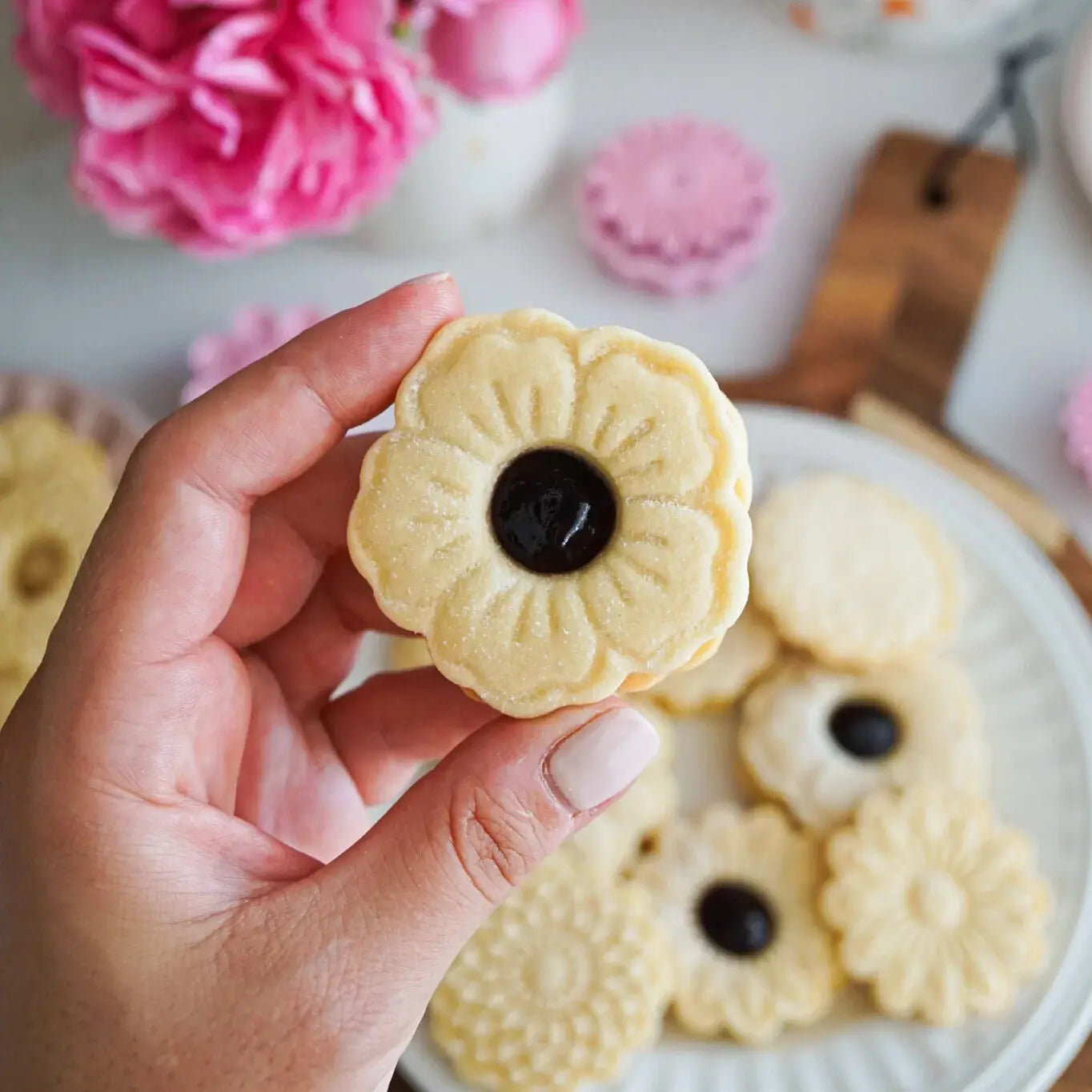 hand holding a flower Linzer cookie with jam filling in the middle