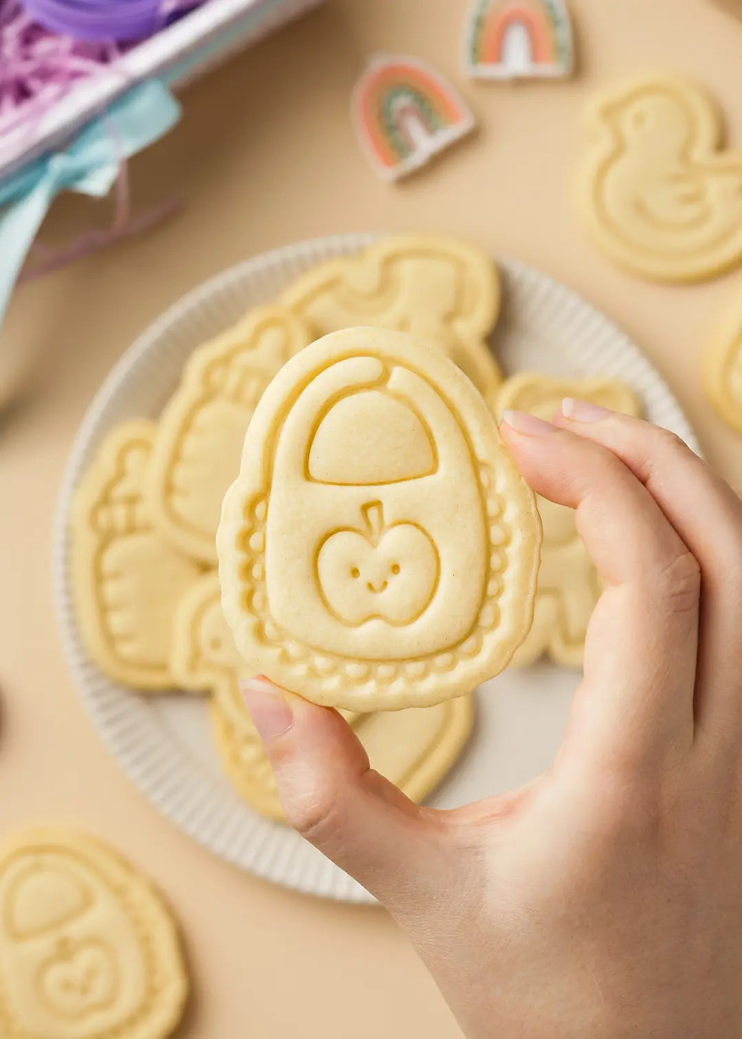 A hand holding a baby shower cookie shaped like a bib with a smiling apple design.