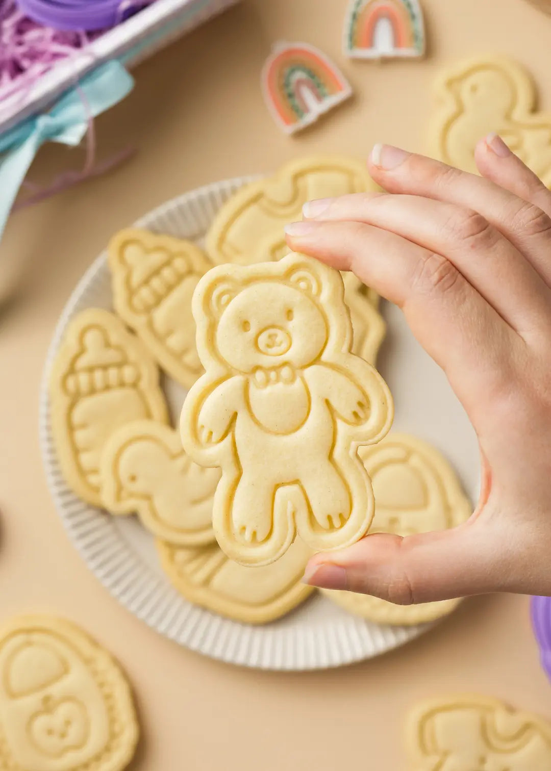 A close-up of a hand holding a teddy bear-shaped sugar cookie, showcasing the fine embossed details.