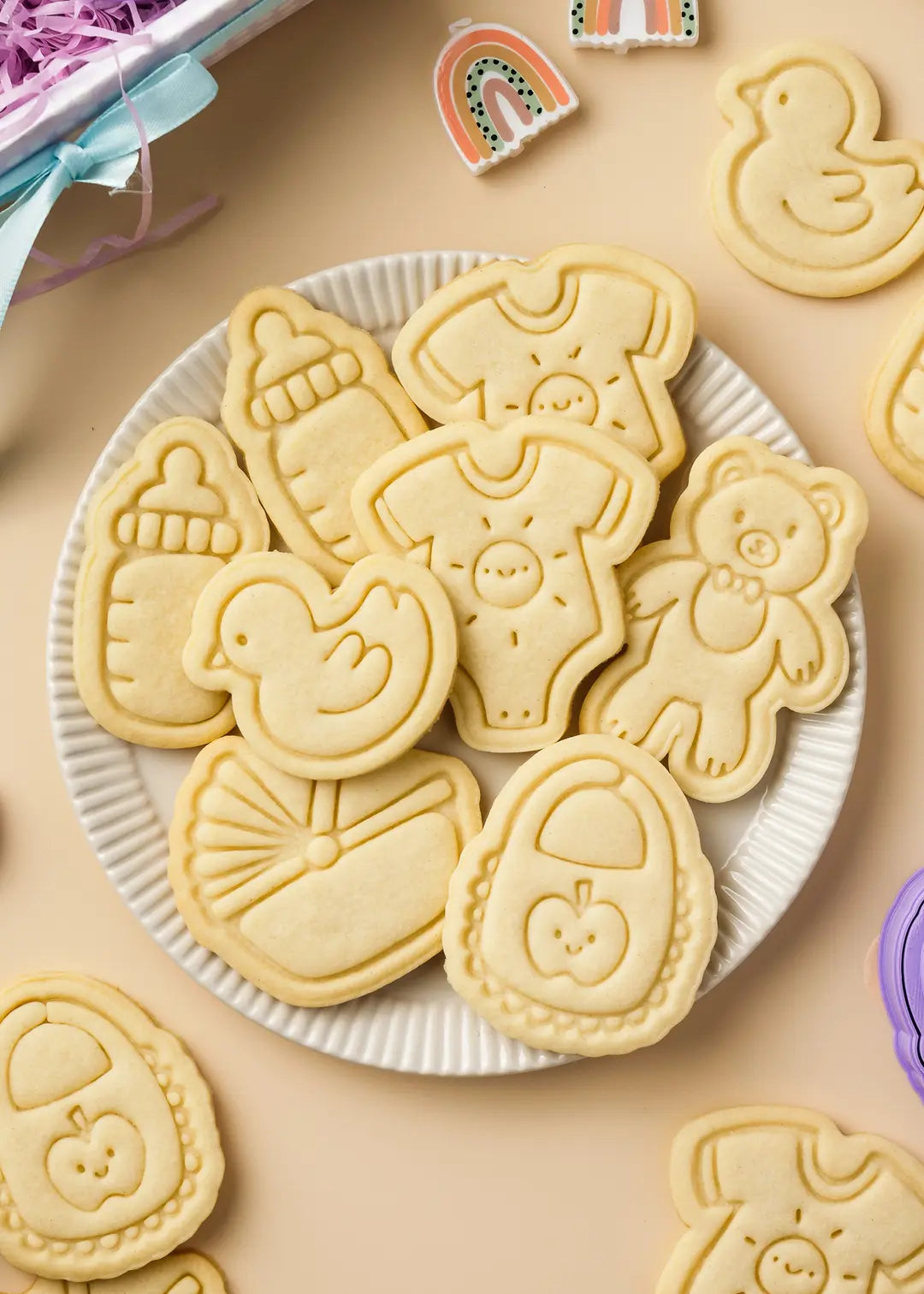 A plate filled with freshly baked baby-themed cookies, including a rubber duck, baby onesie, baby bottle, bib, and bassinet. Made with the baby themed cookie cutter set which is a perfect gift.