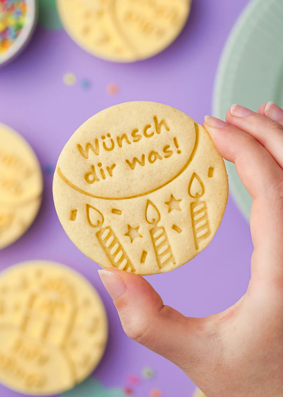 Hand holding a "Wünsch dir was!" birthday cookie – A close-up of a hand holding a wish-themed birthday cookie with candles.