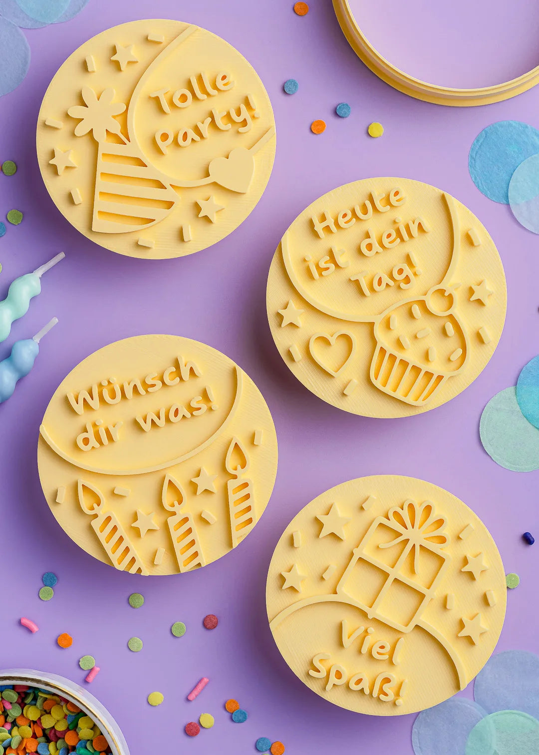 Close-up of four embossed cookie stamps with German birthday messages, including "Tolle Party!" and "Wünsch dir was!", surrounded by colorful confetti.