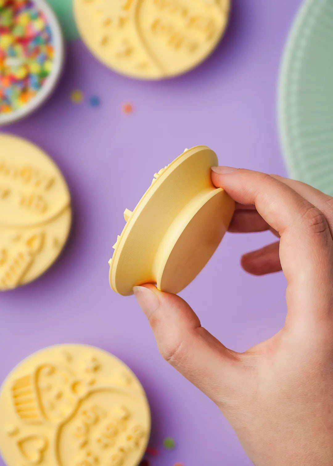 A hand holding a yellow 3D-printed cookie stamp, showing the depth and ergonomic grip of the handle.