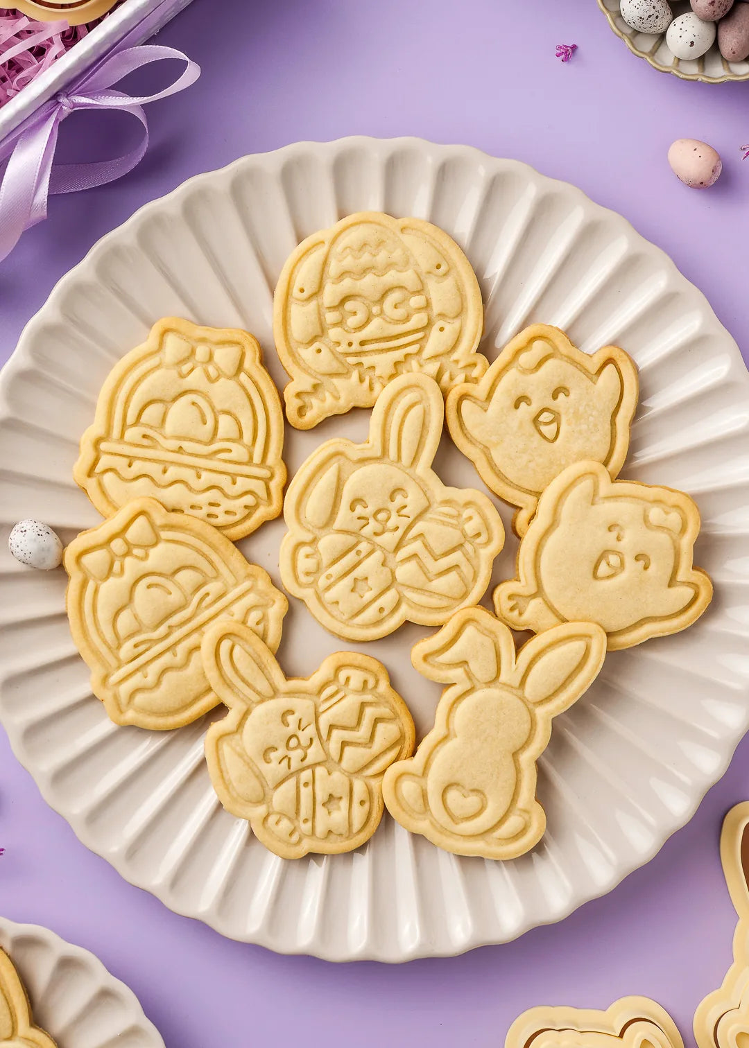 Close-up of decorated Easter cookies on a fluted ceramic plate. Handmade cookies shaped like a bunny, chick, and Easter eggs, perfect for holiday baking.