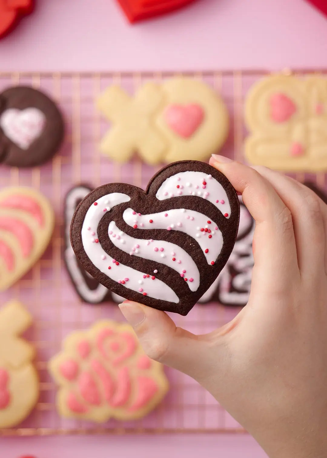 Chocolate heart cookie with icing for Valentine's Day – A hand holding a heart-shaped chocolate cookie decorated with white icing and pink sprinkles, making it a perfect sweet treat for celebrating love.