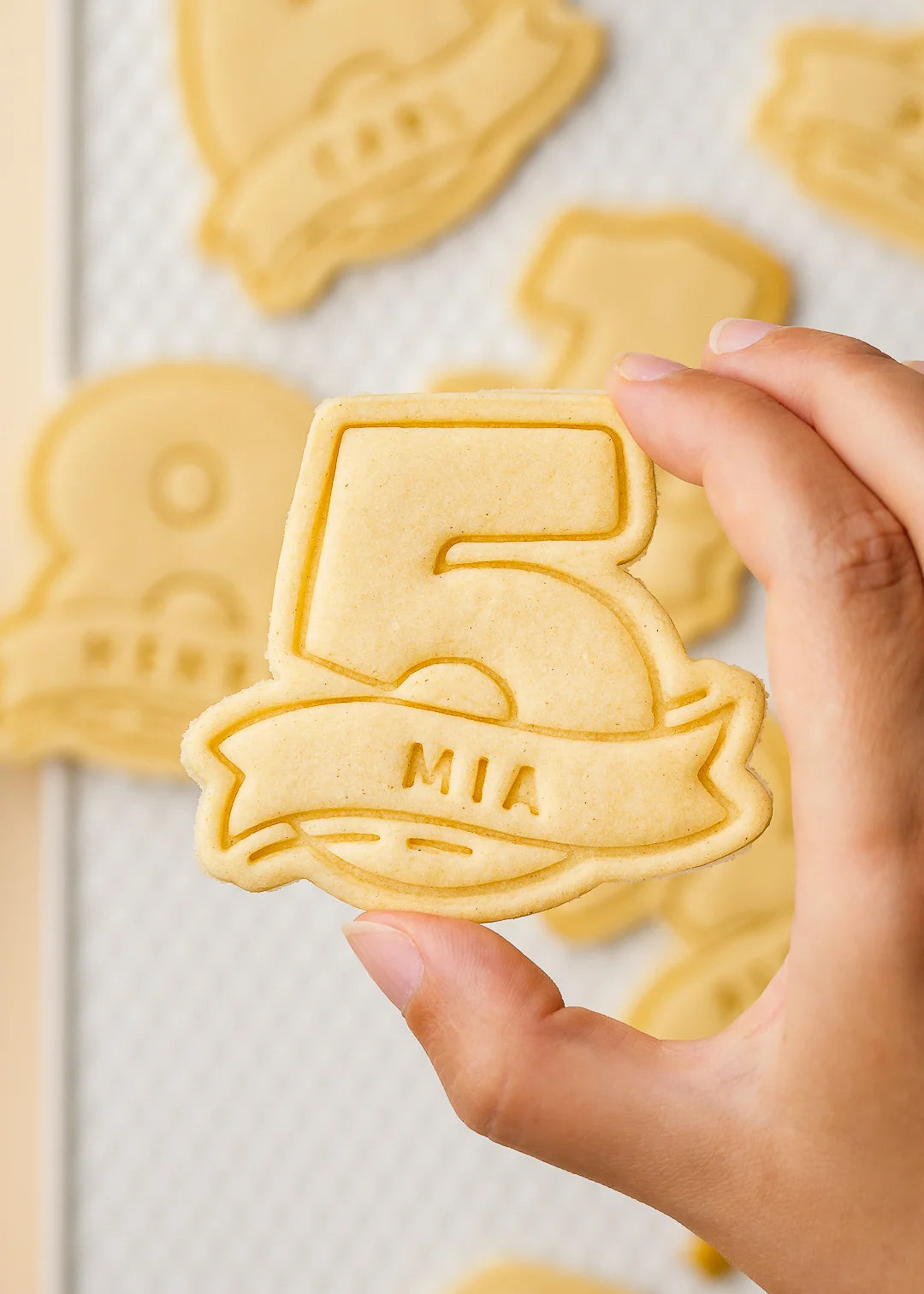 Close up of a custom kids birthday cookie in number five shape with name 'Mia', made with a personalized cookie cutter. Shows perfect baking results and detailed embossing for special occasions.