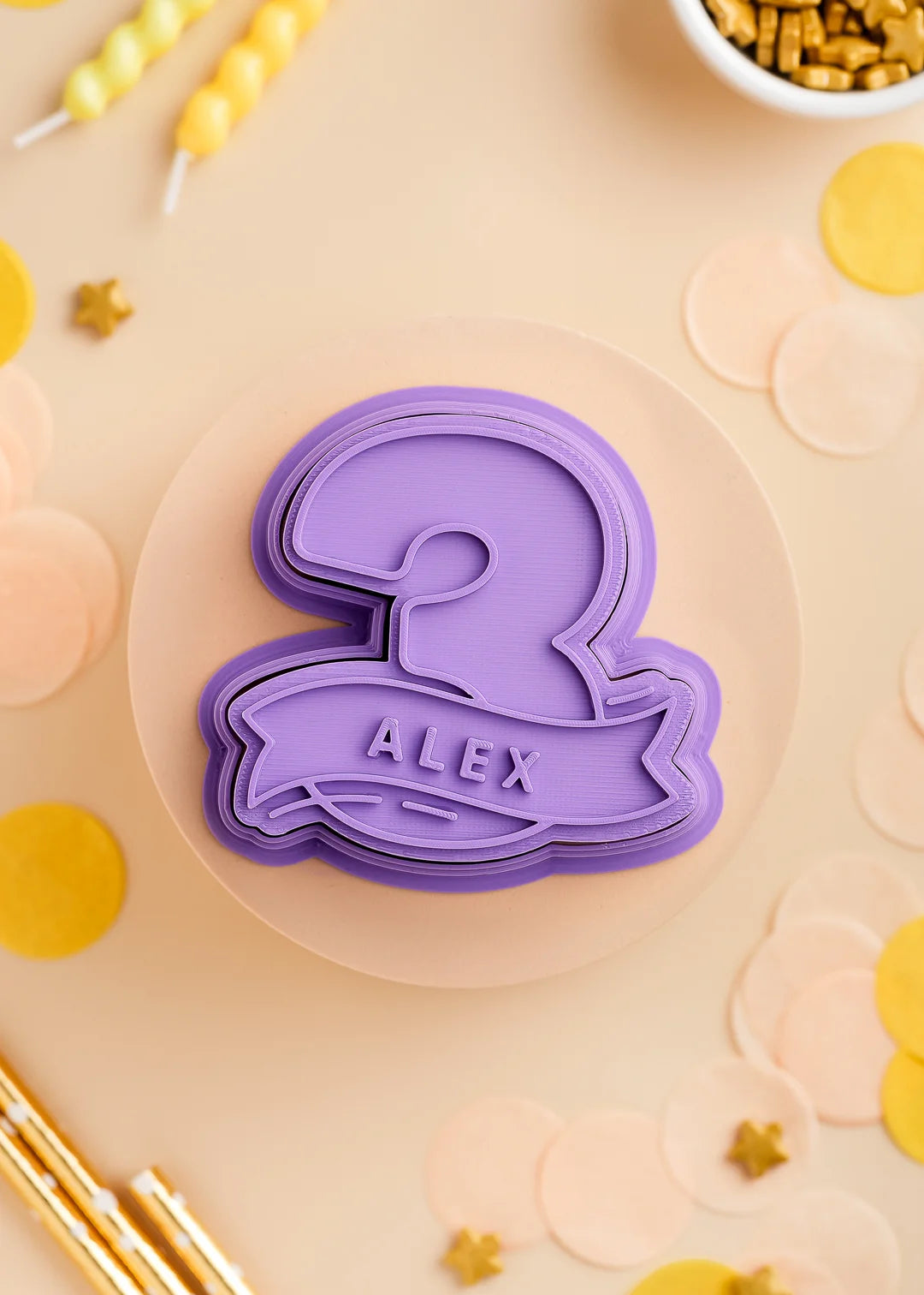 Purple number three cookie stamp with cutter with custom name 'Alex', perfect for a kids birthday party. Surrounded by pastel confetti and party-themed decorations.