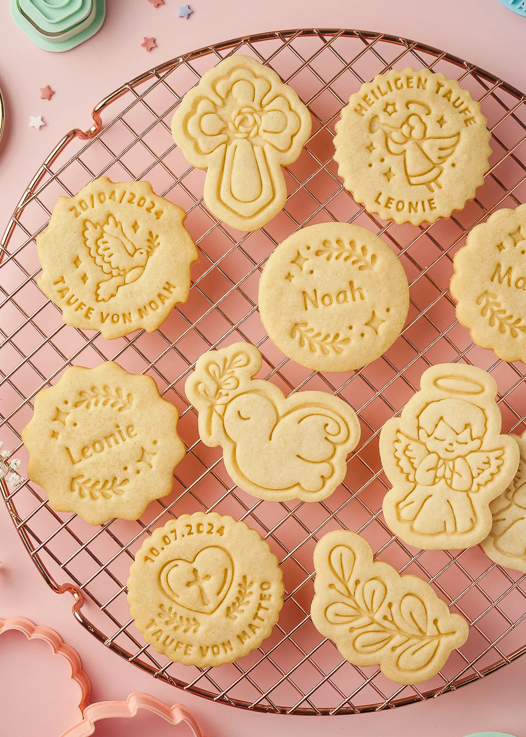 close-up of baked cookies arranged on a cooling rack featuring our customizable designs and the cookie cutter set from our Baptism collection - custom round cookies with names, angles, cross with rose, dove, etc