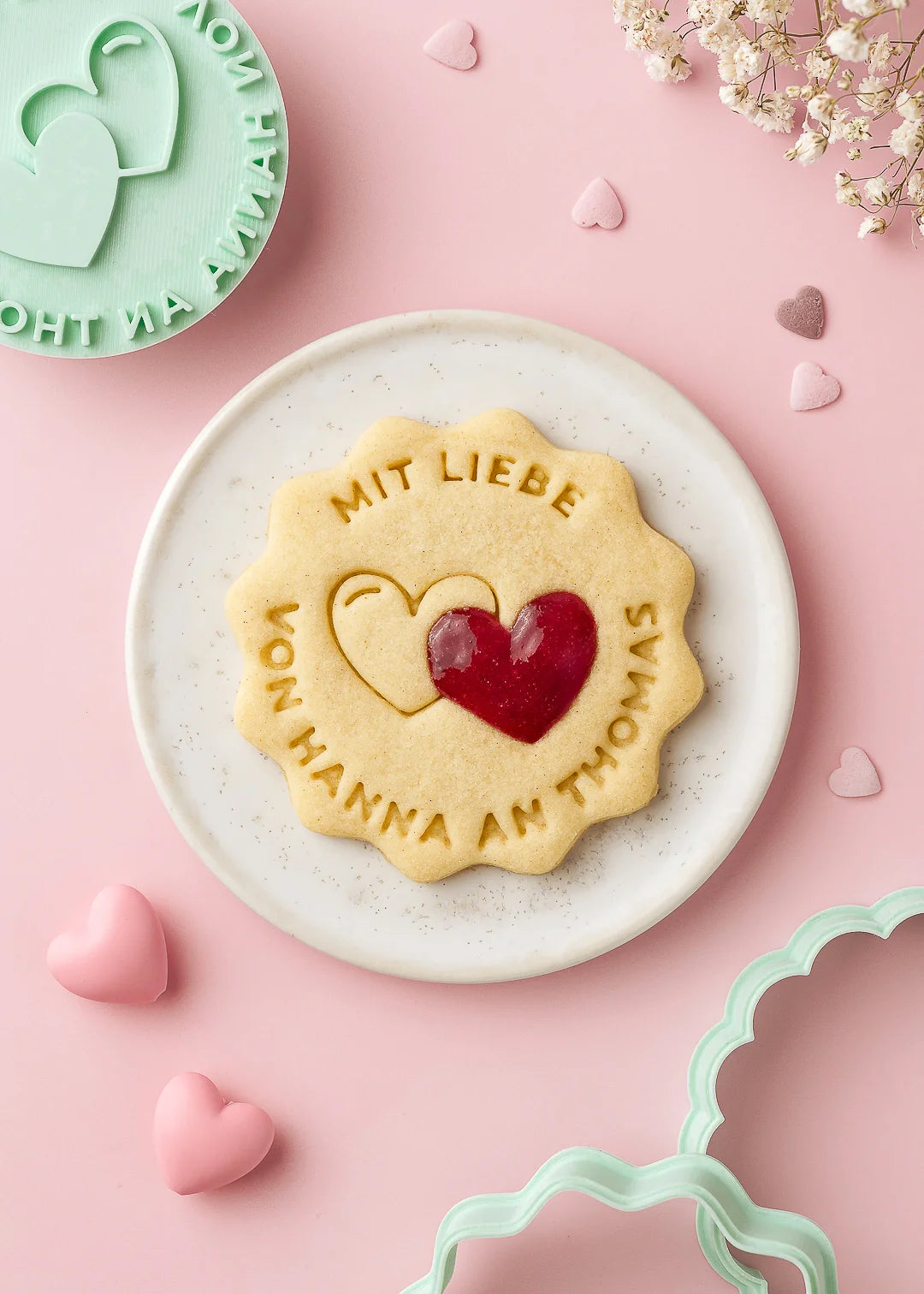 Personalized cookie with the text “Mit Liebe – Von Hanna an Thomas” and two heart shapes, one filled with jam. Made using our custom cookie stamp and cutter – a sweet and thoughtful gift or heartfelt addition to any present.