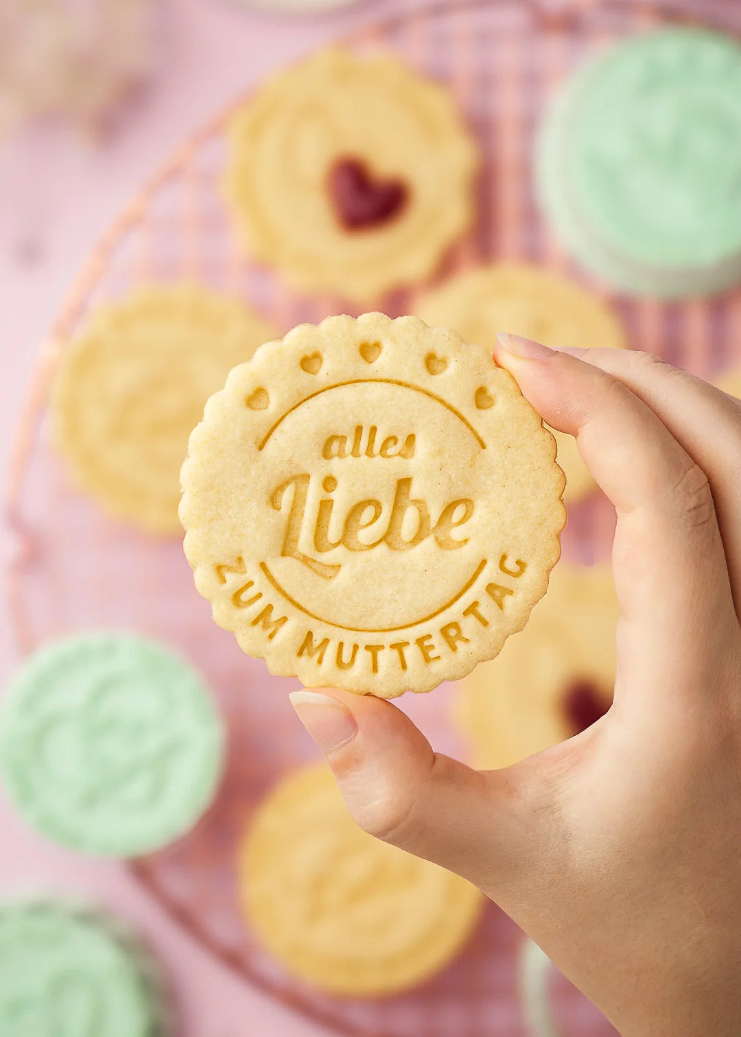 Hand holding a cookie stamped with the German message “Alles Liebe zum Muttertag”, surrounded by small hearts. Made with our custom cookie stamp – a sweet idea for Mother’s Day gifts and homemade treats. Perfect complementary gift.