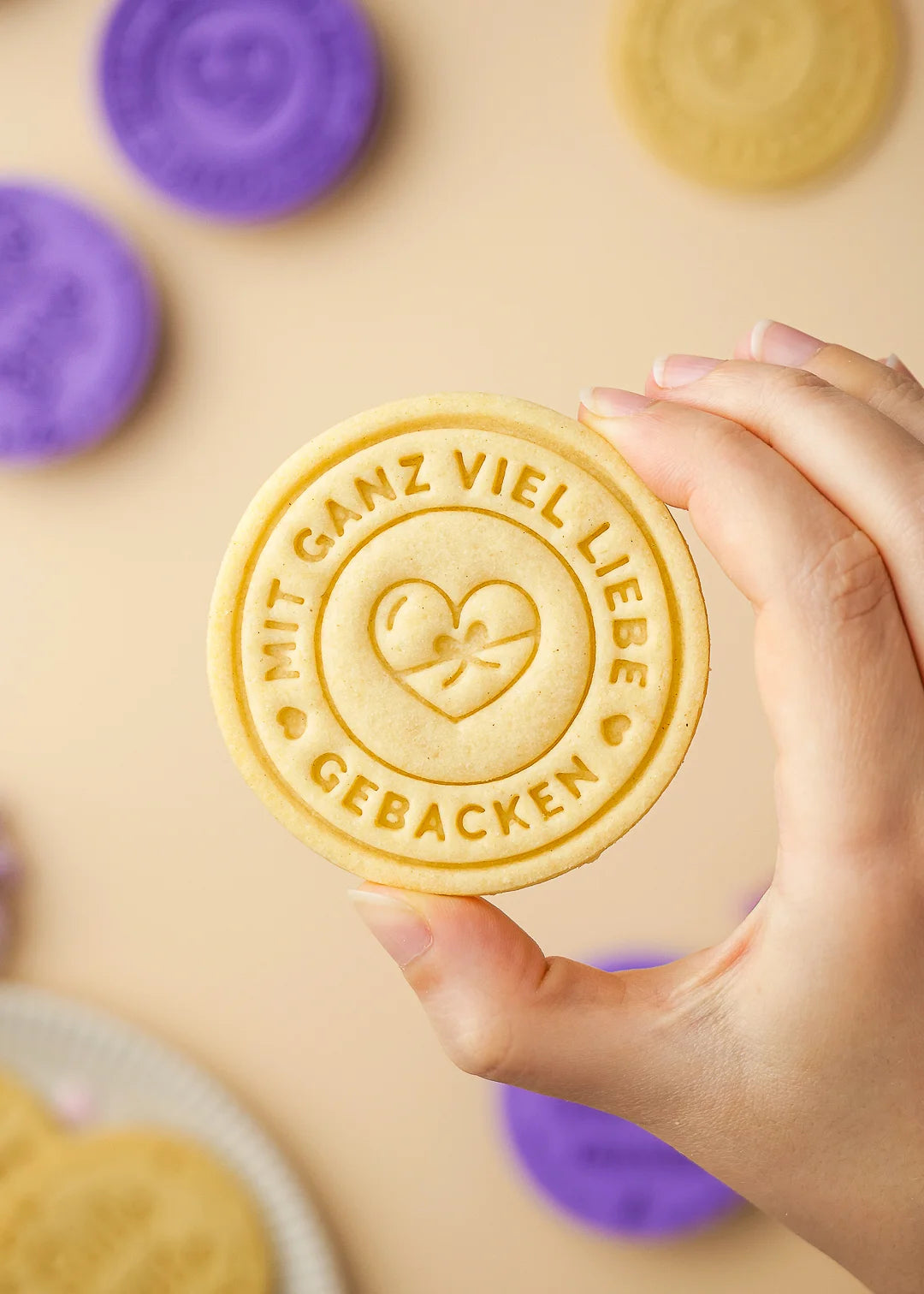 Hand holding a cookie stamped with the German phrase “Mit ganz viel Liebe gebacken” – made using our custom cookie stamp. Clean, detailed impression with a heart and bow design.