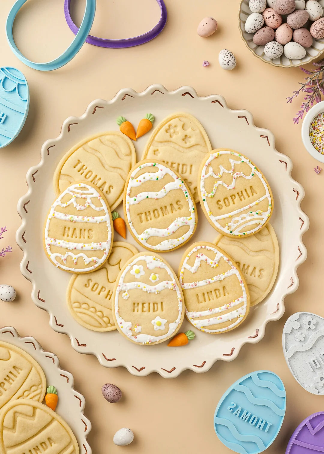 Plate of baked Easter egg cookies with various names. The cookies are decorated with icing and colorful sprinkles.