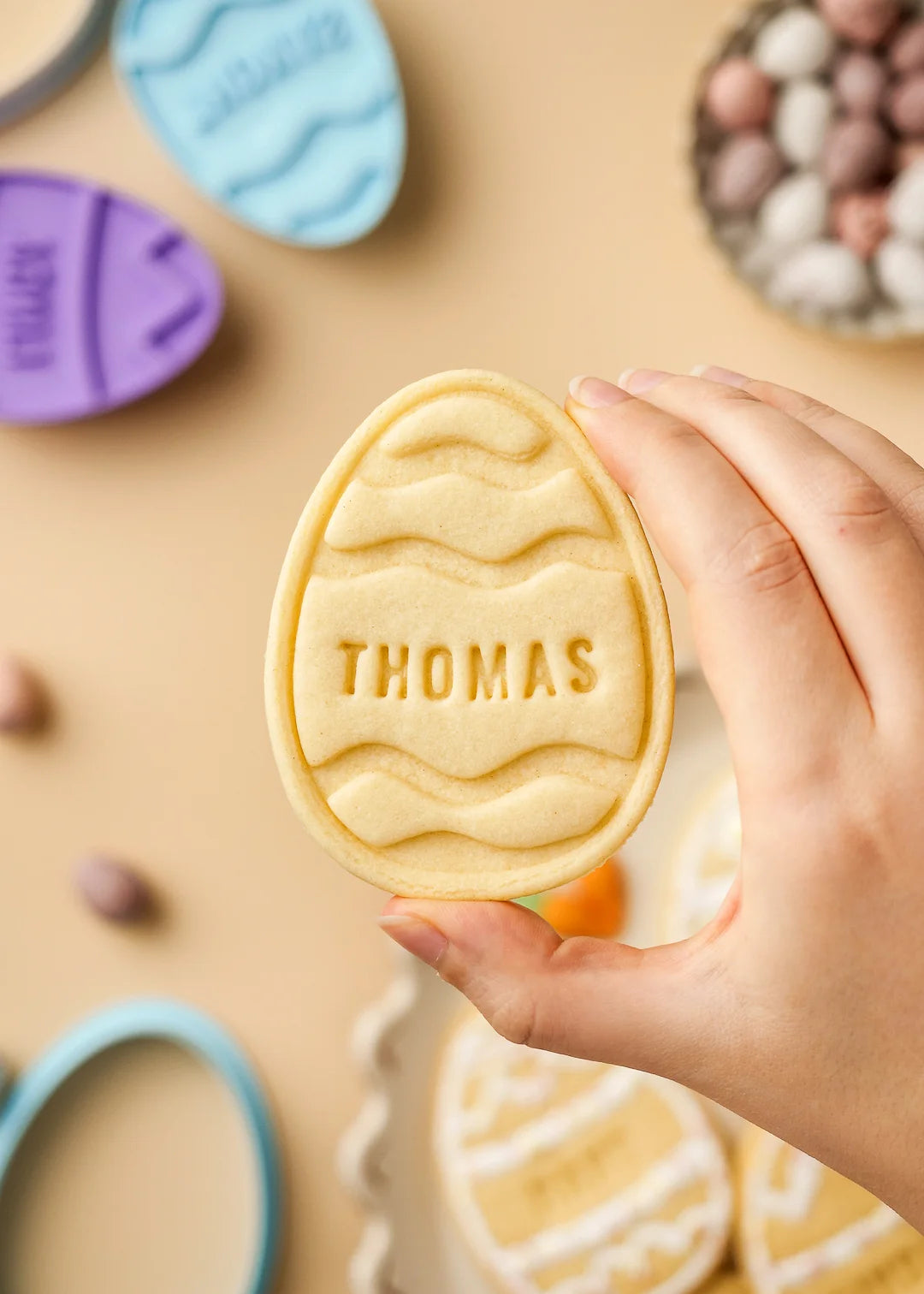 Hand holding a personalized Easter egg cookie with wavy pattern design and name Thomas