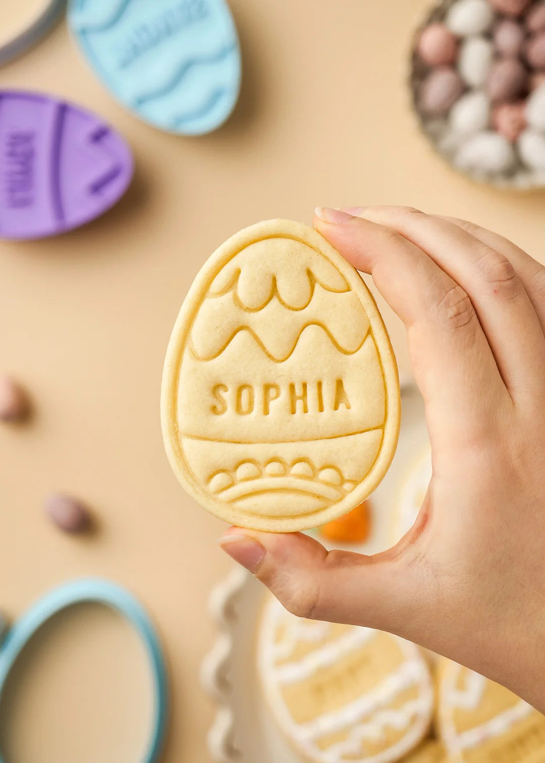Hand holding a personalized Easter egg cookie with swirls pattern design and name Sophia