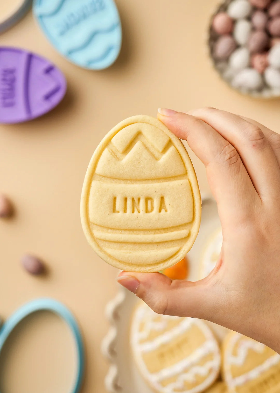 Hand holding a personalized Easter egg cookie with zigzag pattern design and name Linda