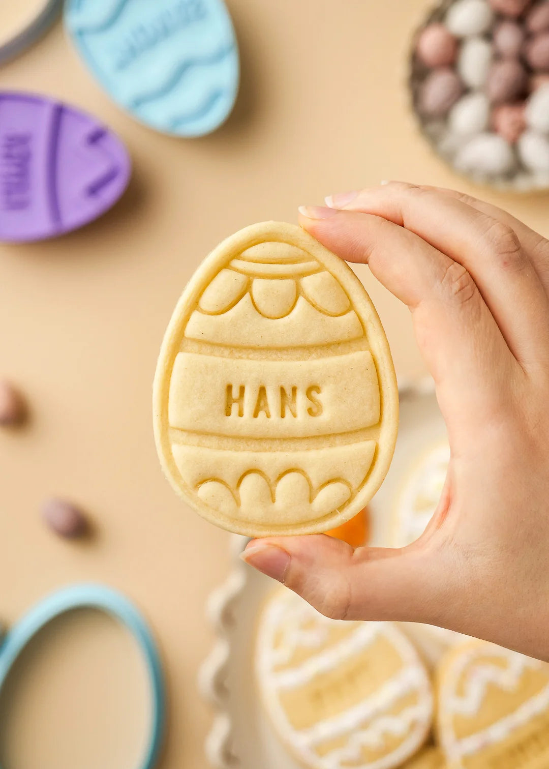 Hand holding a personalized Easter egg cookie with scalloped pattern design and name Hans
