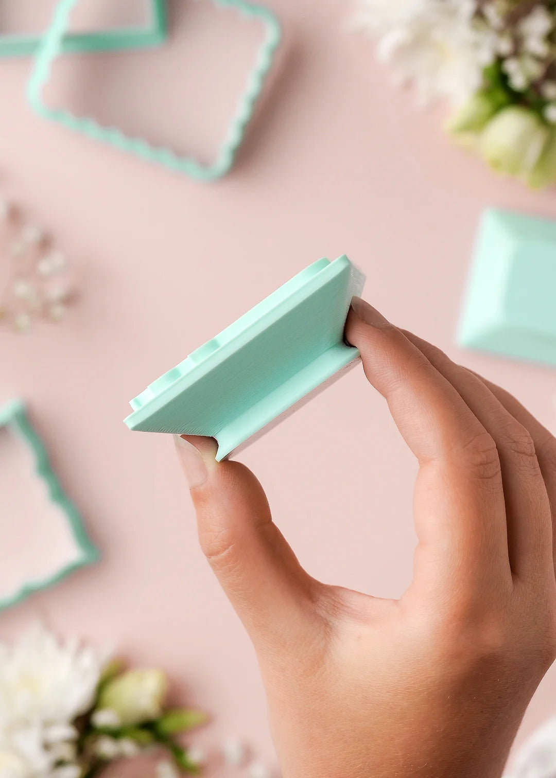 Hand holding a rectangular wedding cookie stamp with built-in handle, shown with matching cookie cutters.