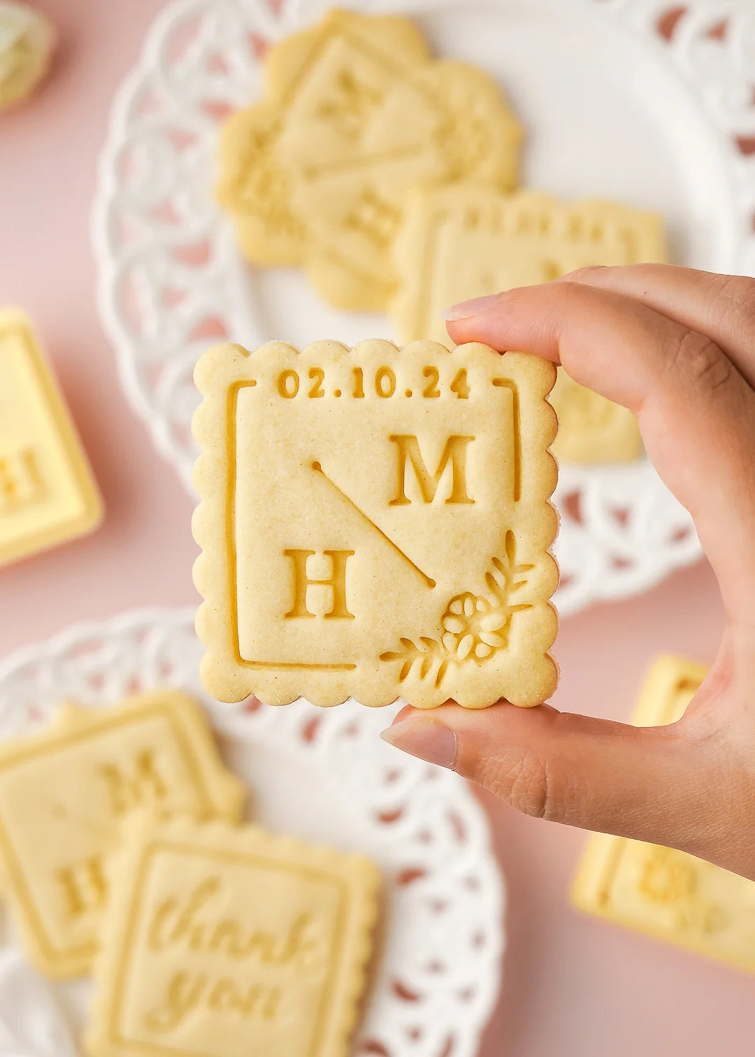 Baked cookie with initials M&N and date 02.10.24, made with custom wedding square cookie stamp and a scalloped square cookie cutter.