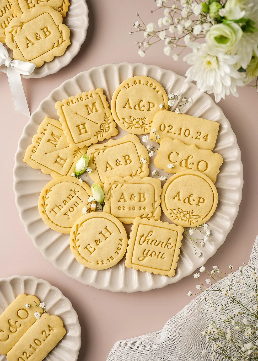 Wedding-themed personalized cookies displayed on elegant ceramic plates, showcasing various custom cookie stamp designs including round, square, and rectangular shapes. Each cookie features options like initials, wedding date, couple’s names, or thank you messages, made with Formini’s customizable cookie cutters and stamps – perfect for wedding favors and gifts.