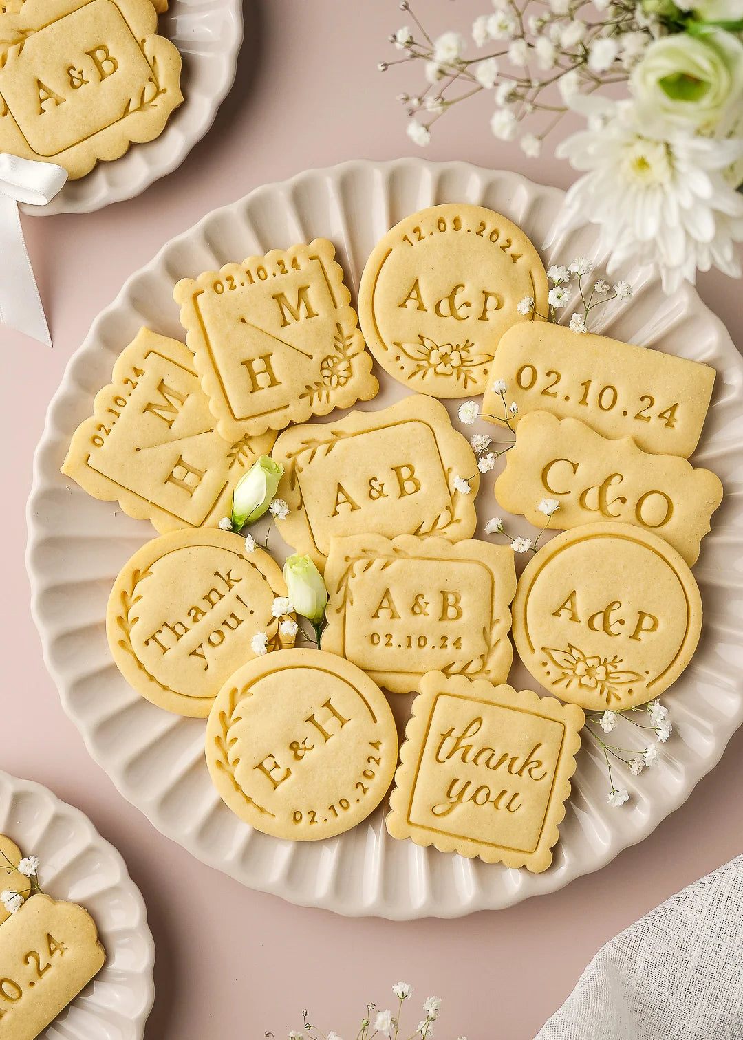 Close-up of wedding-themed personalized cookies displayed on elegant ceramic plates, showcasing various custom cookie stamp designs including round, square, and rectangular shapes. Each cookie features options like initials, wedding date, couple’s names, or thank you messages, made with Formini’s customizable cookie cutters and stamps – perfect for wedding favors and gifts.