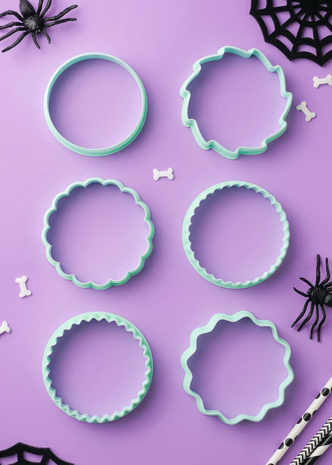 6 green cookie cutters on a purple background with Halloween decorations. Different edge styles - wavy, scalloped, star, etc. Choose your favorite shape.