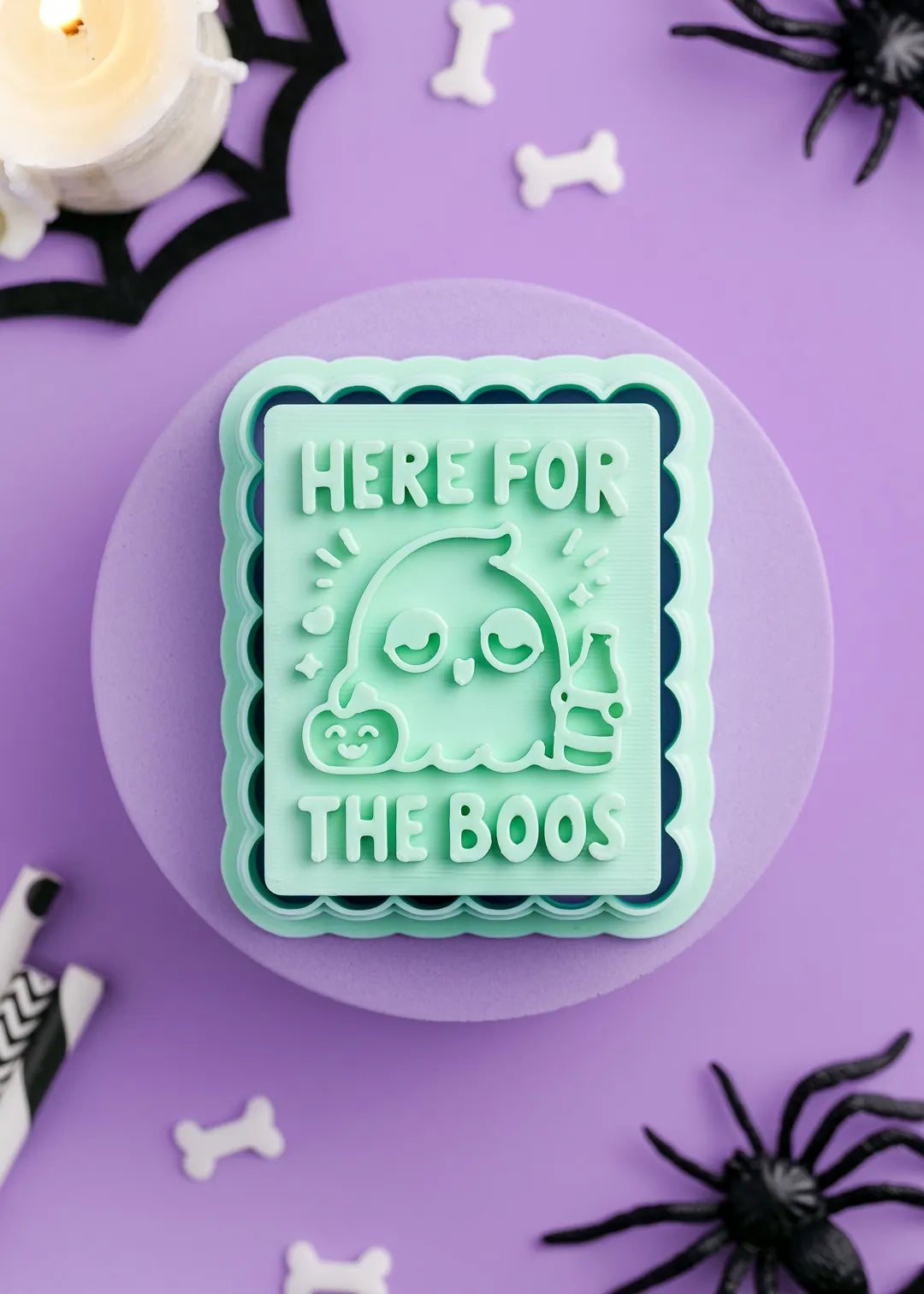 Green Halloween-themed cookie stamp with text "Here for the Boos" and a tipsy ghost holding a bottle on a purple background with spider decorations.