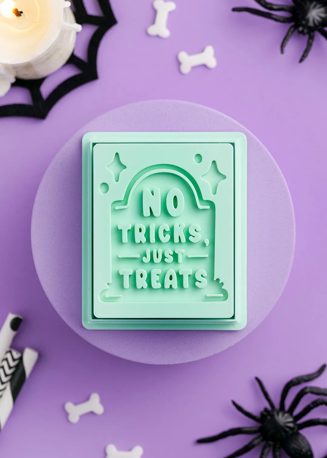 Green cookie stamp with 'No Tricks, Just Treats' text on a purple background with Halloween decorations.