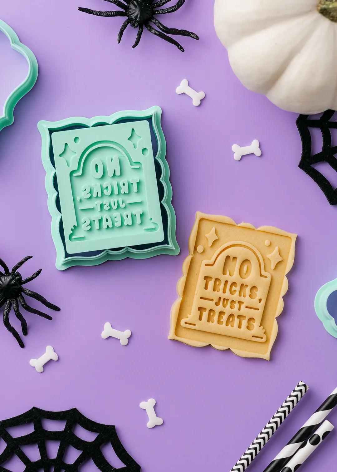 Halloween-themed cookie stamp with "no tricks just treats" text on a purple background with spider webs and pumpkins.