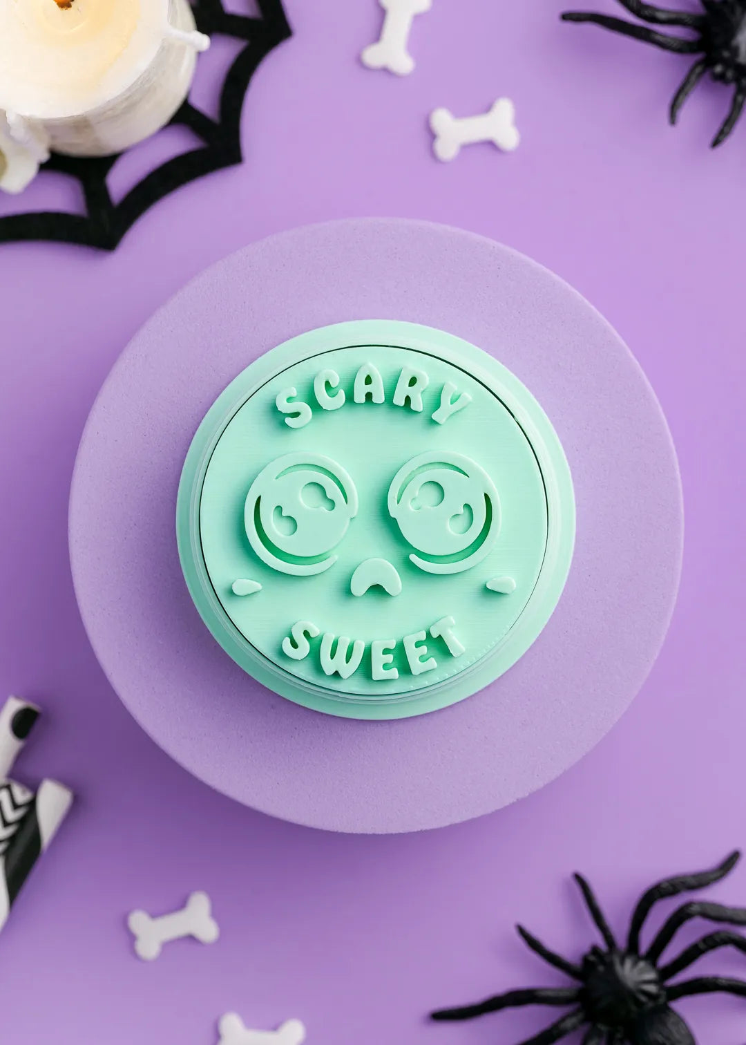 Green cookie stamp with 'Scary Sweet' text on a purple surface with Halloween decorations.