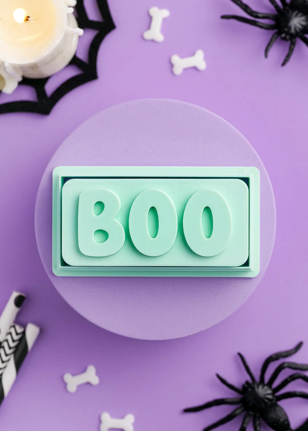 Green cookie stamp with 'BOO' text on a purple background with Halloween decorations.
