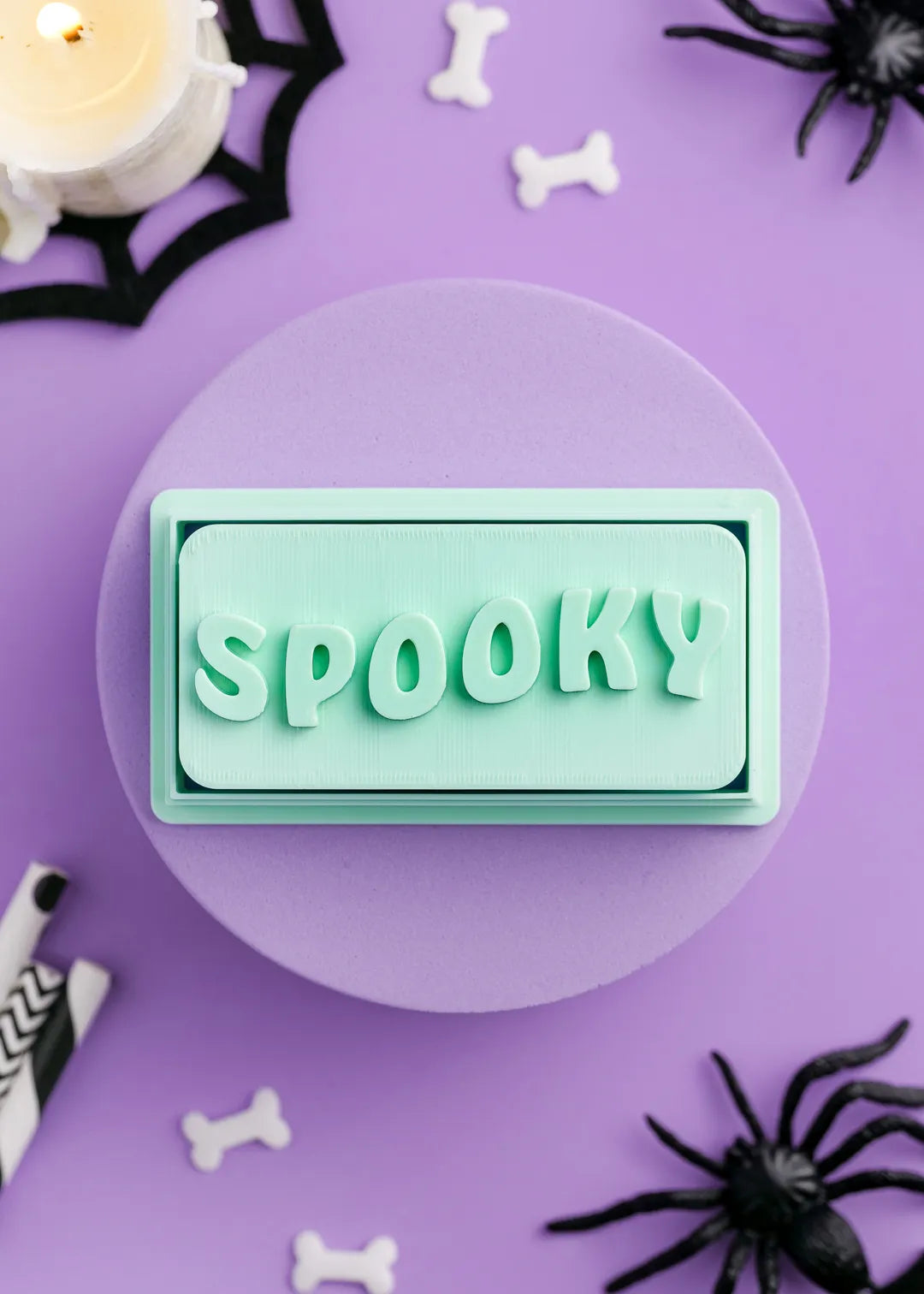 Green cookie stamp with 'Spooky' text on a purple background with Halloween decorations.