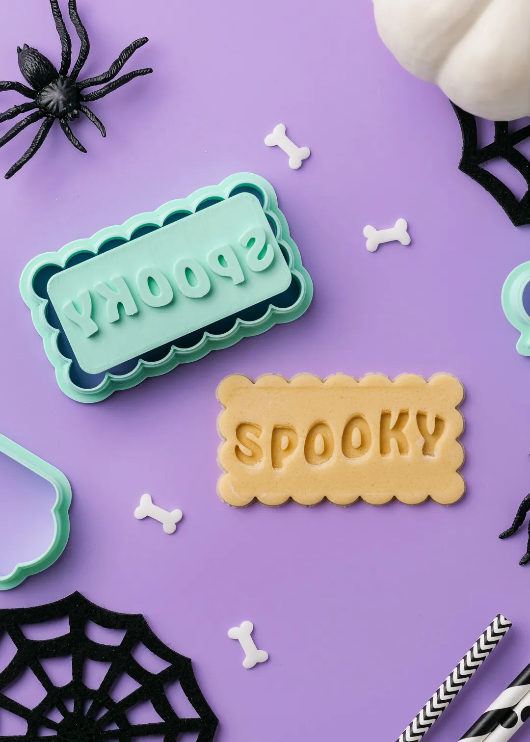 Cookie cutter with 'Spooky' text on a purple background with Halloween decorations.