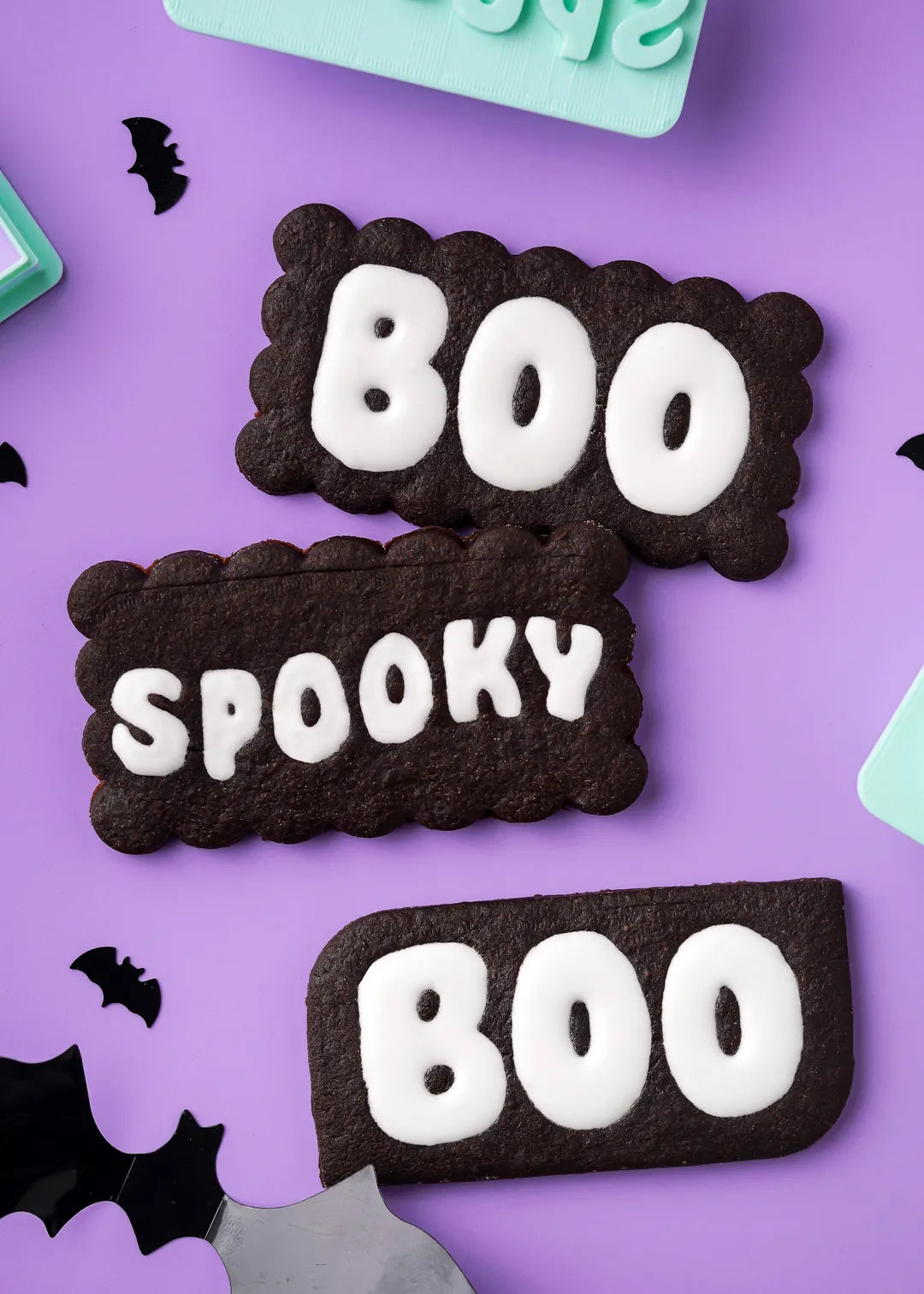 Halloween-themed iced cookies with 'BOO' and 'SPOOKY' text on a purple background.