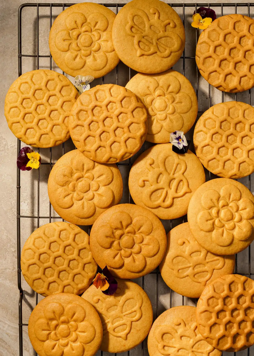 A selection of honey-themed cookies, beautifully arranged on a cooling rack. The intricate stamped designs highlight the delicate details of the bee and honeycomb patterns.